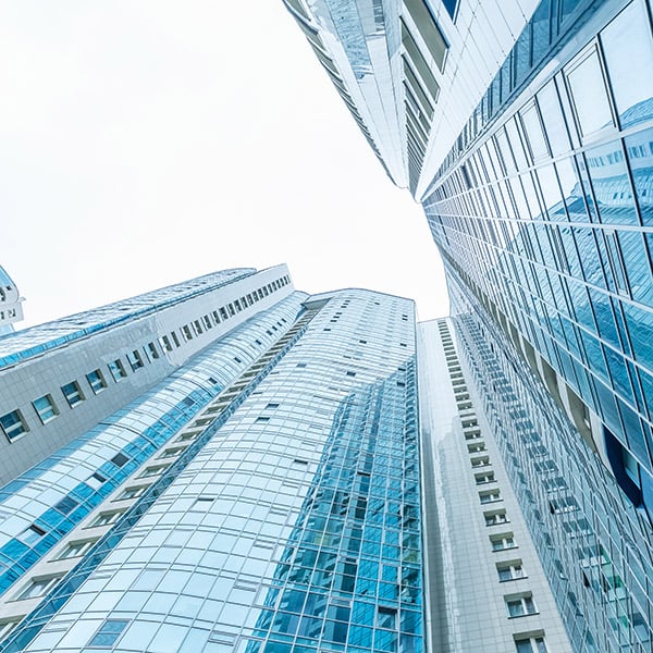 Picture of the view from the ground looking up at multiple tall buildings with blue-tinted glass